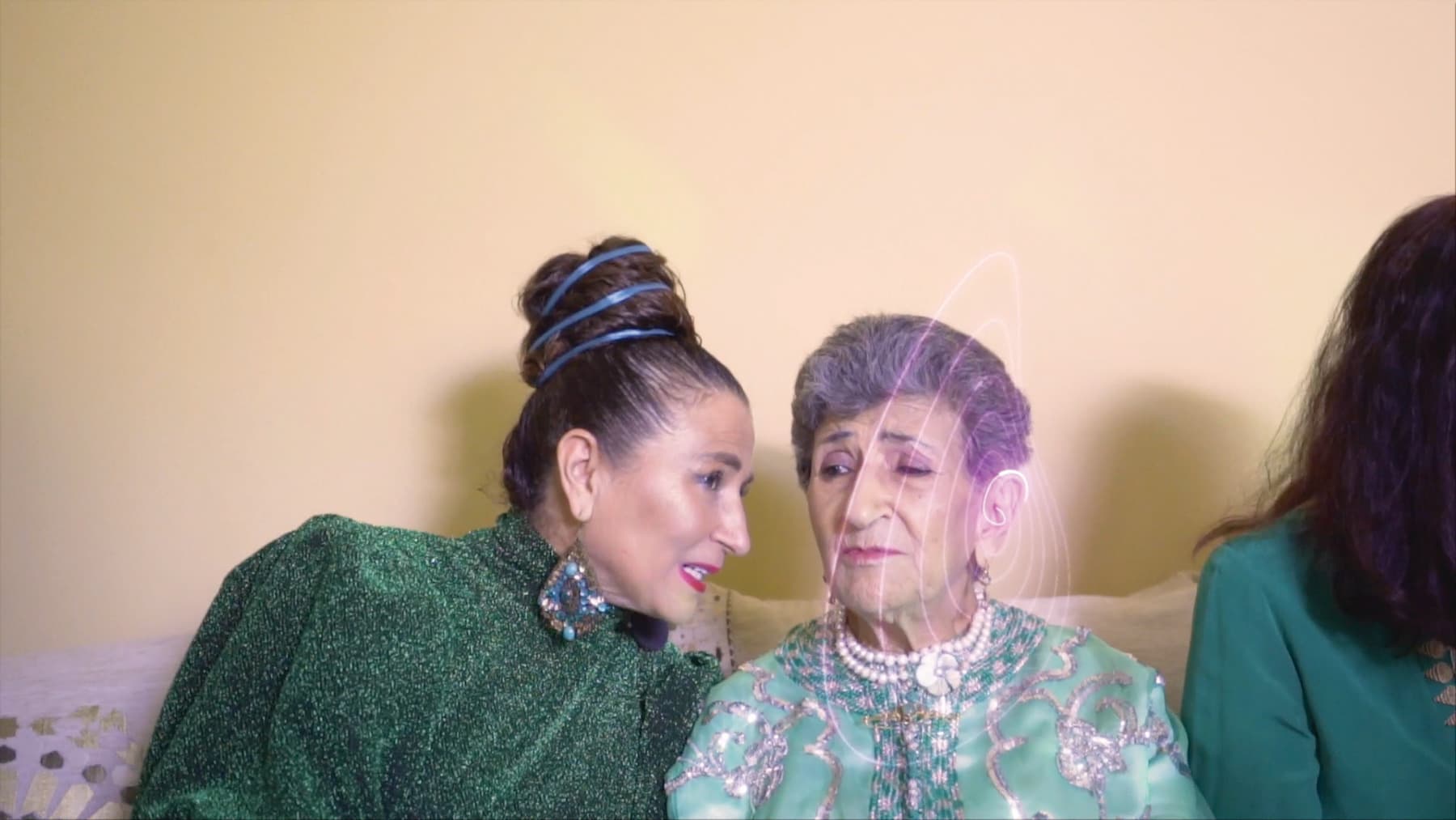 Three women are sitting together. The woman on the left is whispering something to the women in the middle.