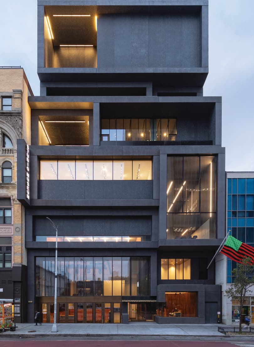The shot of the front of the museum. It is a grey building that is rectangular with boxy architecture and a lot of large windows.