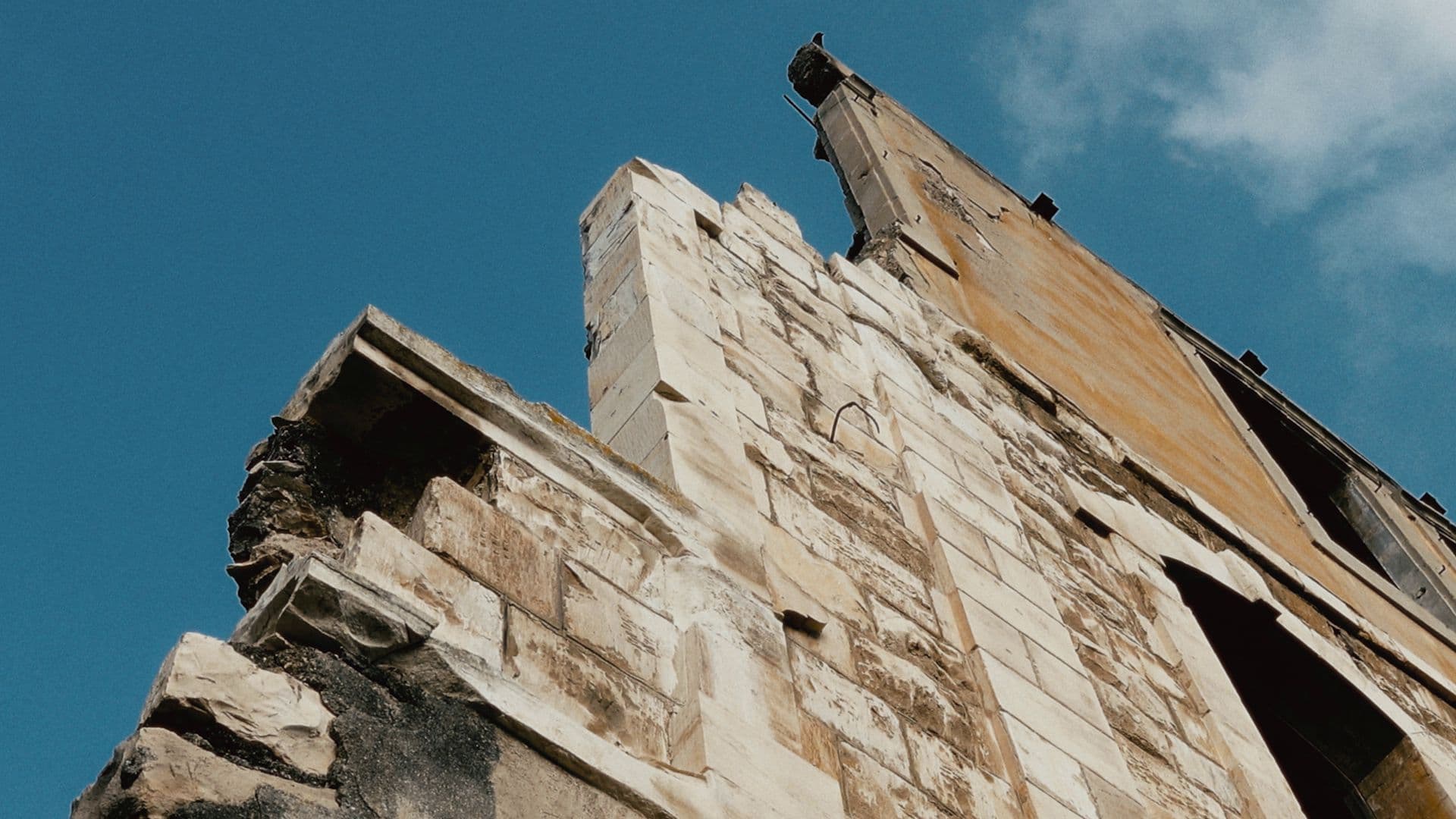 A film still from Another Day Shall Come shows the ruins of a Palestinian house in Wadi Salib, a neighborhood in the city of Haifa. The image shows the side of a worn stone wall with a blue sky in the background.