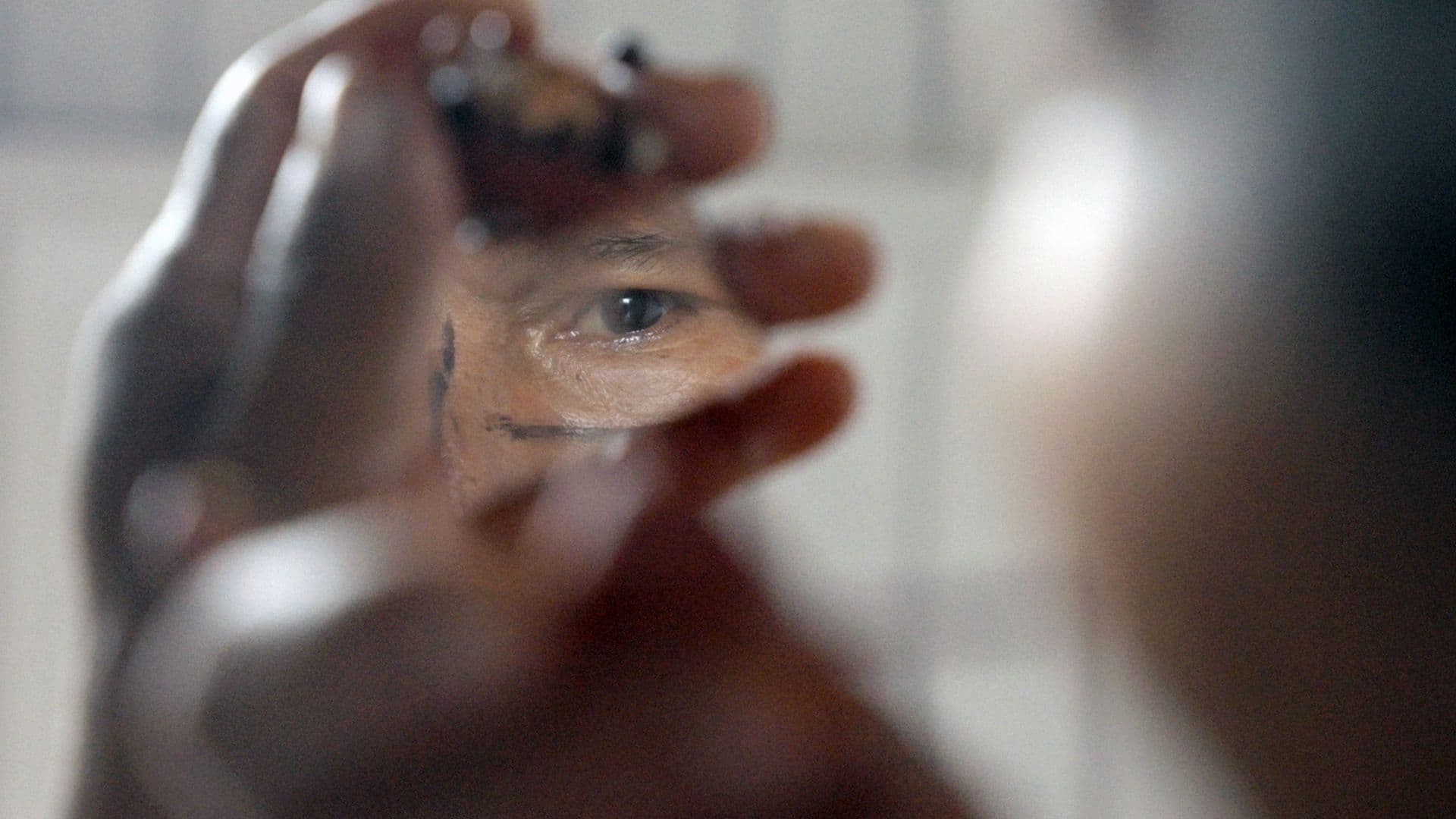 A film still from Charip: Lightning in the River shows an older Wampís man holding a mirror shard that reflects his eye.