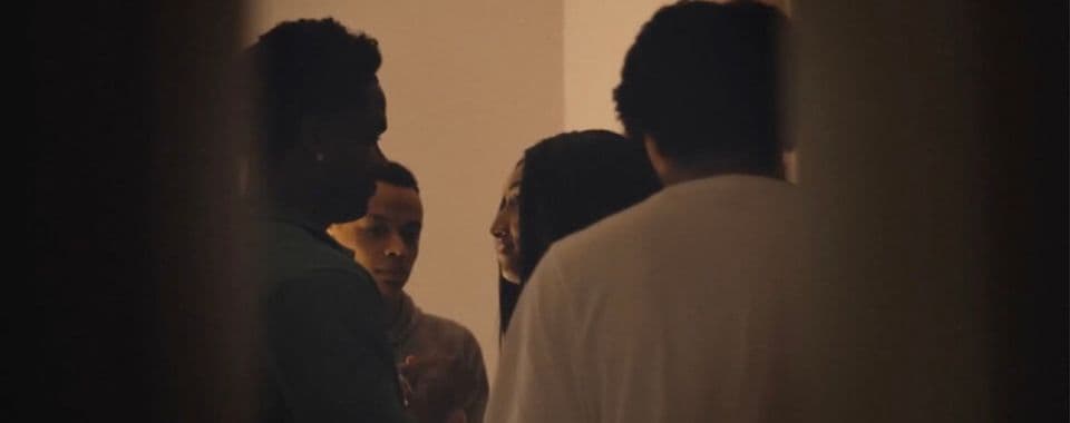 A film still from Free Lyric shows a teenage Black girl surrounded by three teenage Black boys in a room.