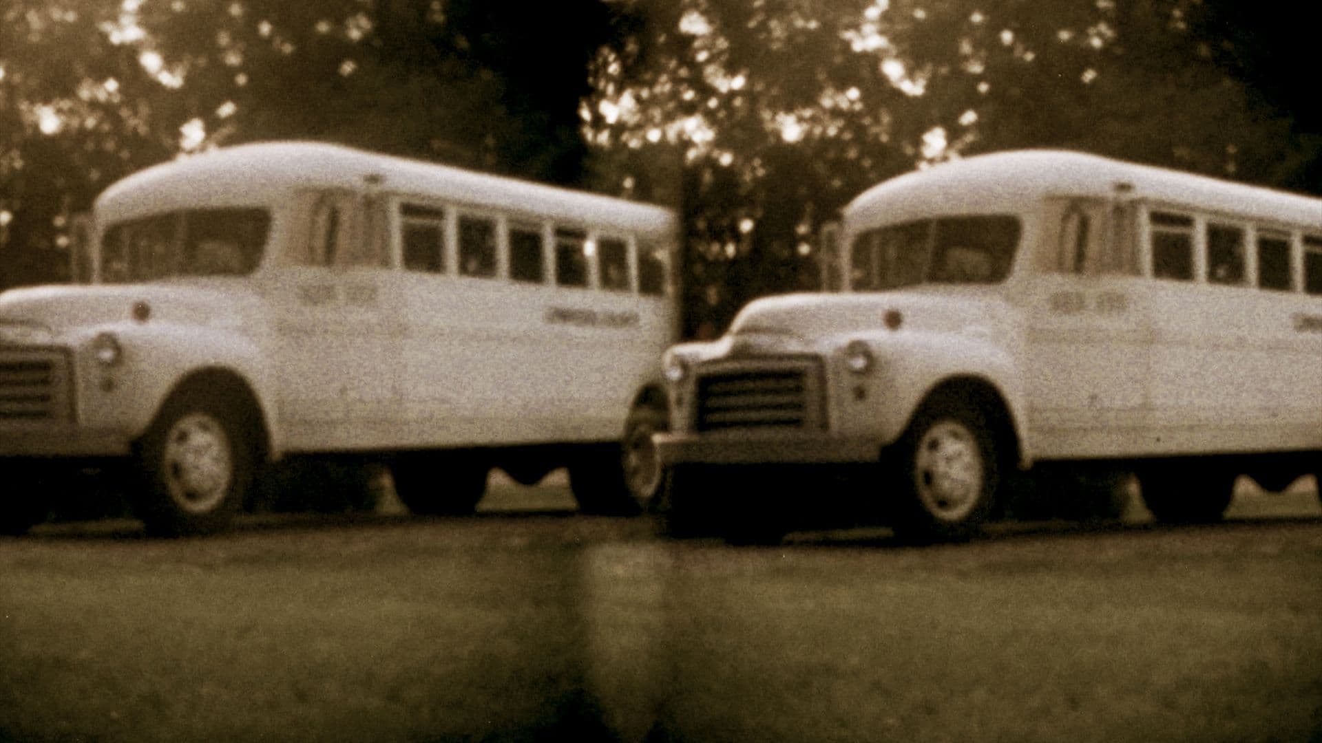 A sepia-toned still from National Seating shows two school buses parked side-by-side on a driveway, surrounded by grass and trees.