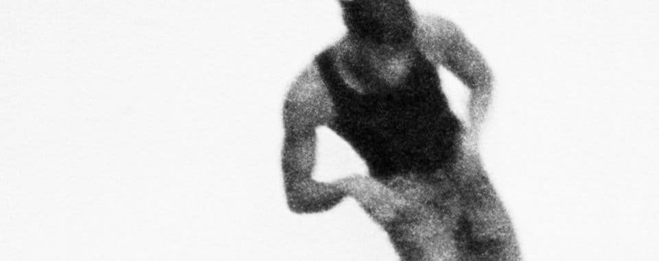 A black-and-white film still from Revival 24 shows a blurred figure of a Black man dancing mid-motion against a black background. The man is wearing a black tank top, jeans, and a dark-colored durag.