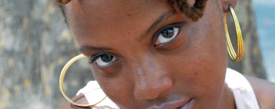 A film still from Scene Not Heard: Women in Philadelphia Hip Hop shows a close-up of a young Black woman with gold hoop earrings looking up at the camera.