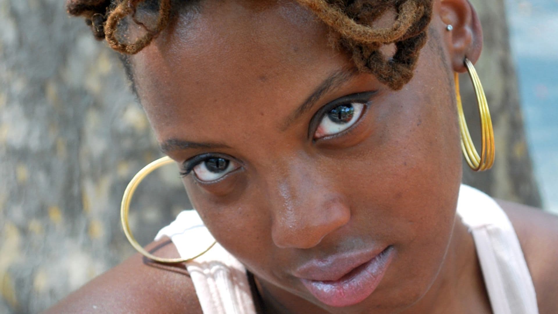 A film still from Scene Not Heard: Women in Philadelphia Hip Hop shows a close-up of a young Black woman with gold hoop earrings looking up at the camera.