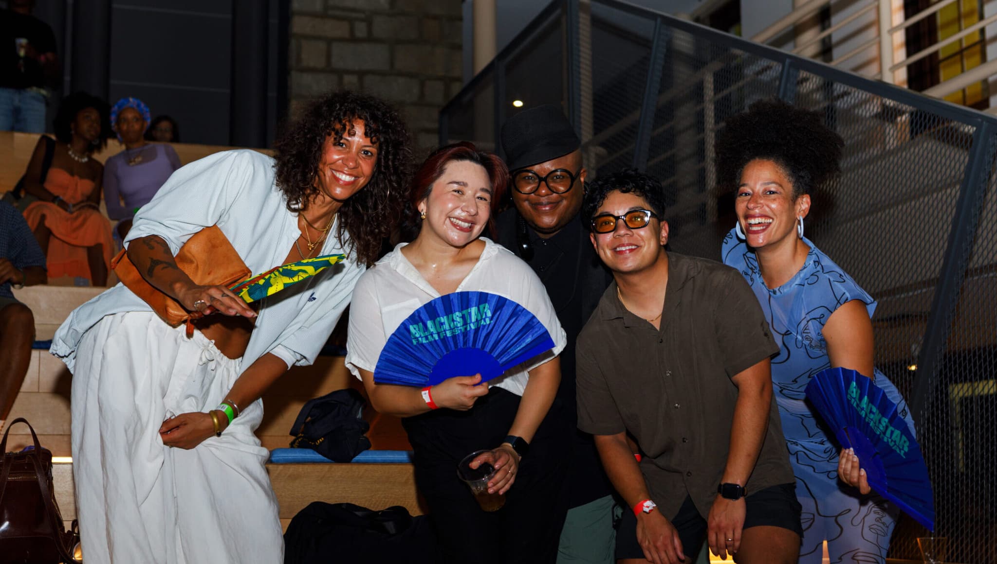 A group of people posing for a photo at the Opening Night Party. They are holding blue BlackStar Film Festival fans and smiling.