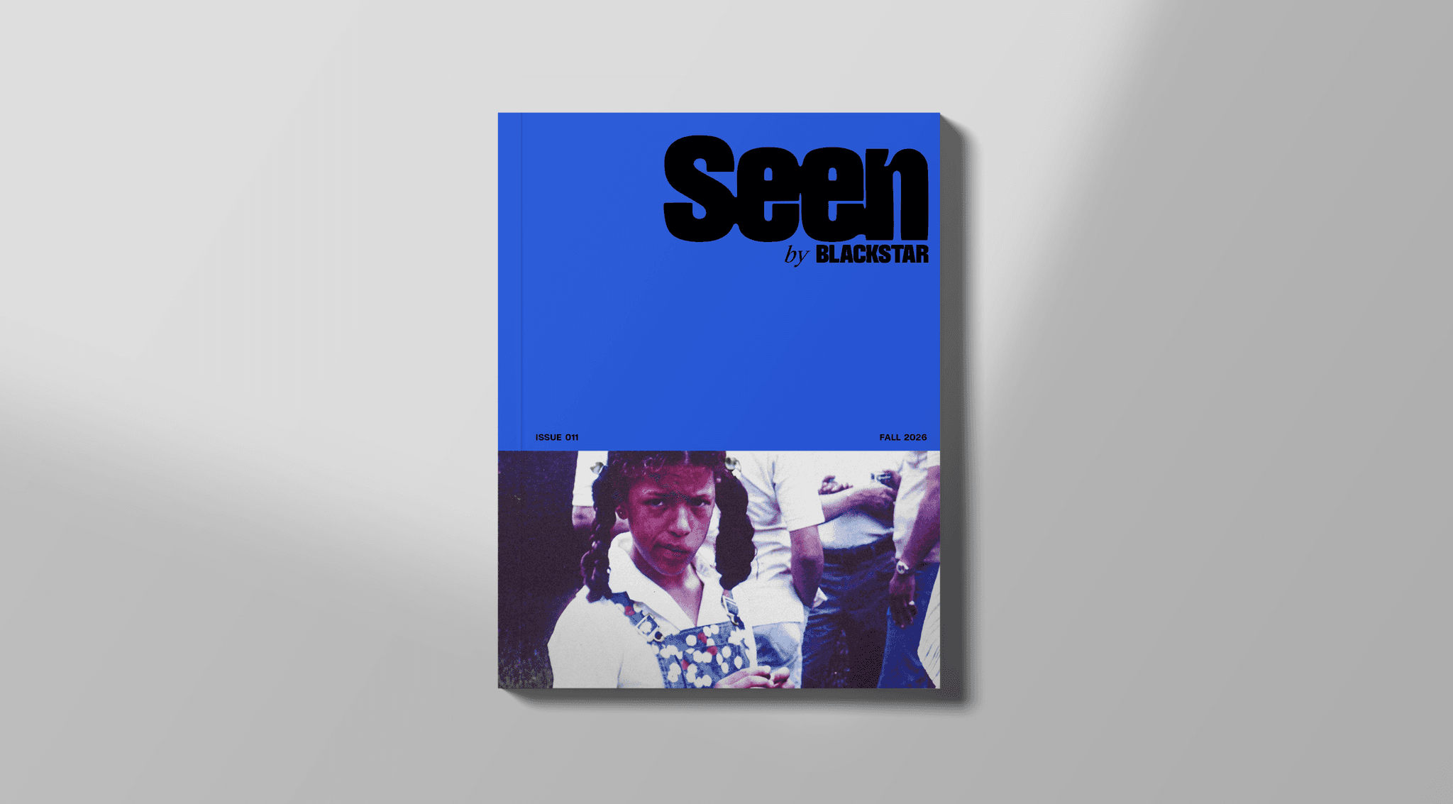 An image of the Seen Issue 011 cover. The top half of it is cobalt blue with the Seen logo in the upper right corner. The bottom half has a photo of Michele Stephenson as a young girl. She is wearing denim overalls with polkadots over a white button down shirt. She has pig tails and a smirk on her face.